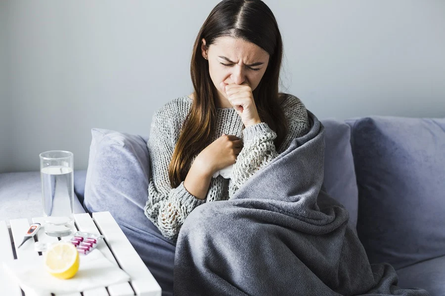Flu-blog Woman with flu symptoms coughing under a blanket at home